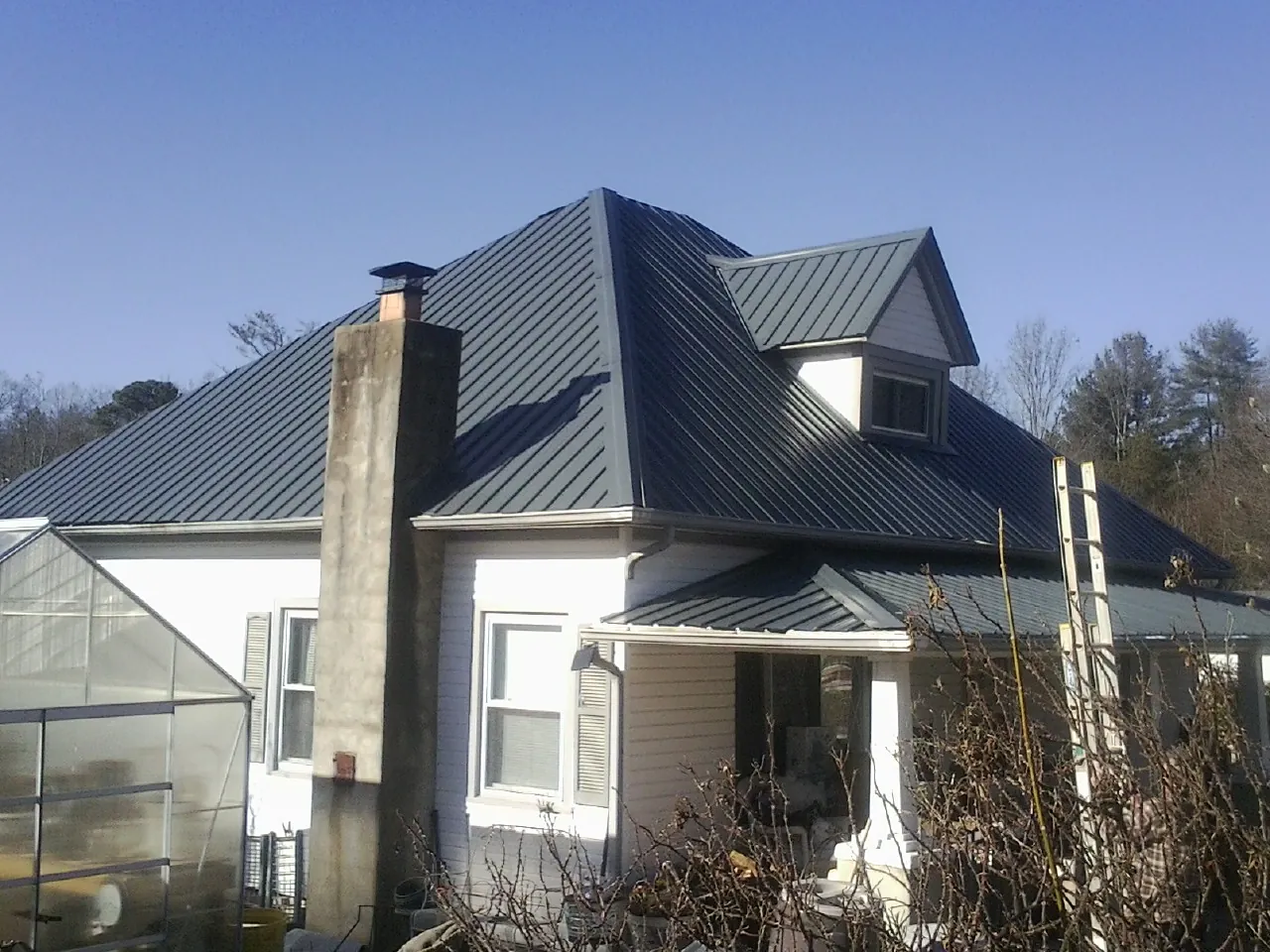Dark blue standing seam metal roof on a white farmhouse with dormer — Slate & Tile Roof Repair by Roofing Brothers in Revloc