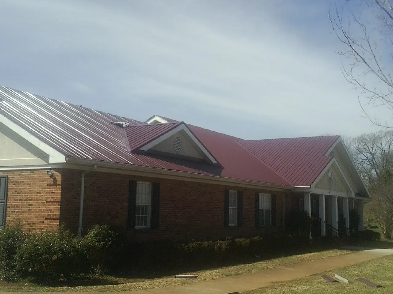 Red metal roof with gabled entries on a long brick building, from a Hail Damage Roof Repair job in Revloc