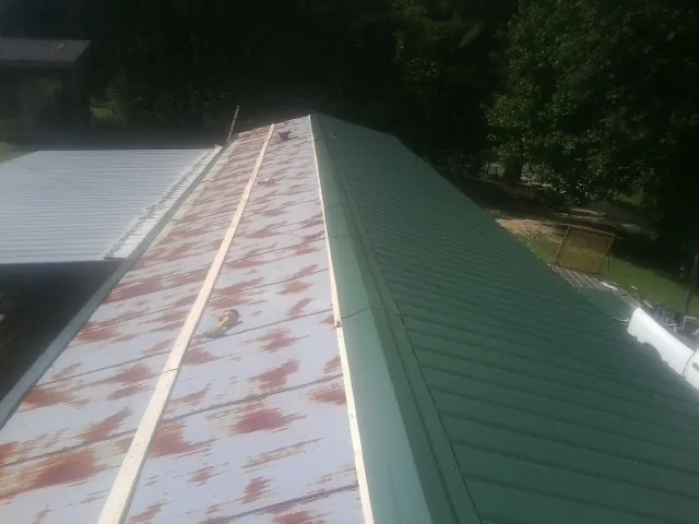 Old rusted panels beside newly installed green metal roofing — Wind Damage Roof Repair by Roofing Brothers in Revloc