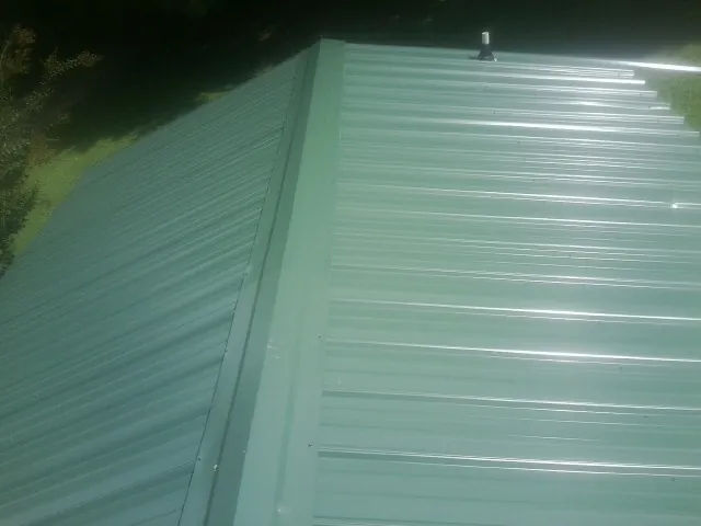 New green metal panels meeting at the ridge of a roof — Flat Roof Repair work by our crew in Revloc
