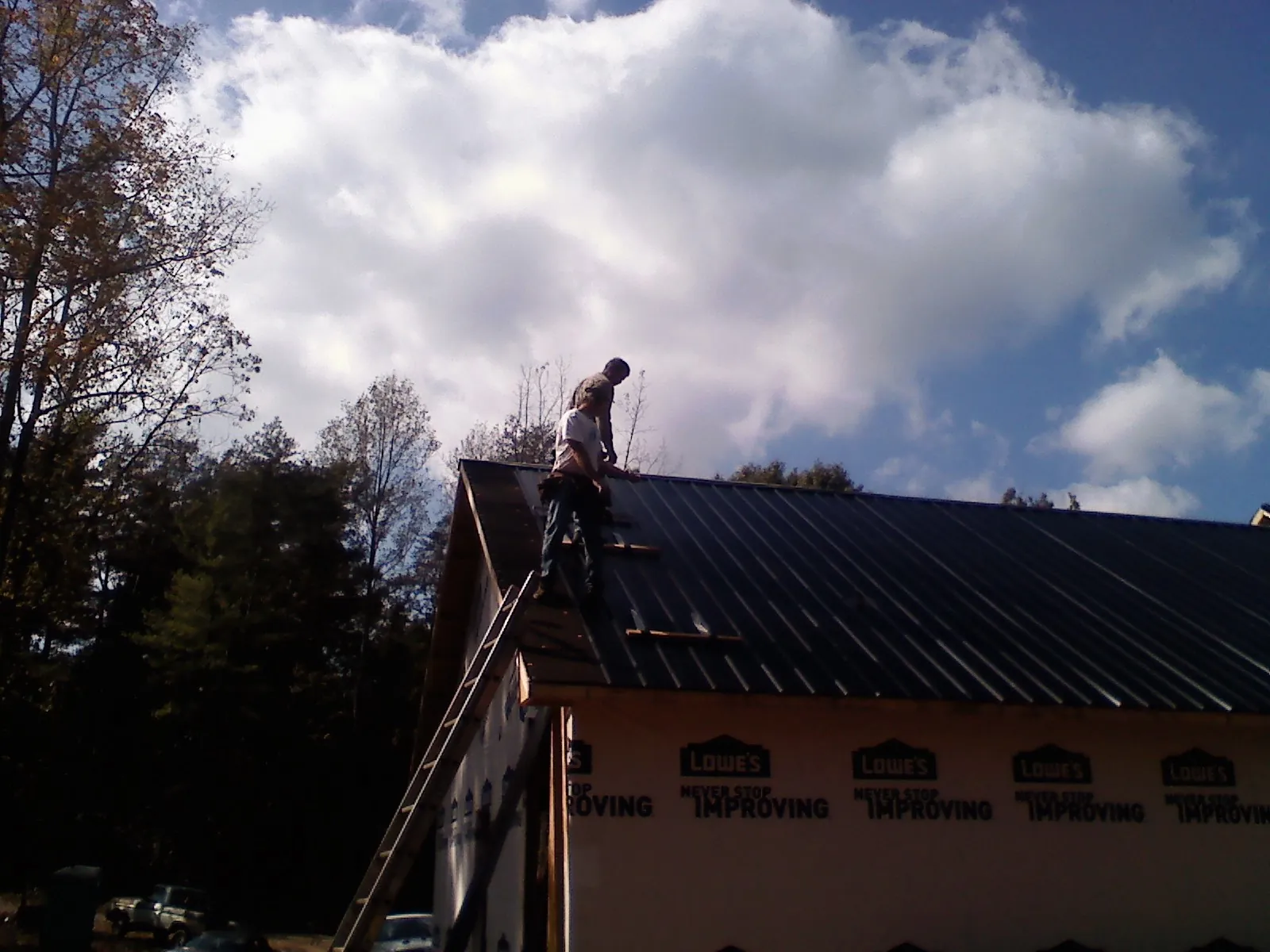Roofer fastening dark metal panels high against a cloudy sky, from a Roof Inspection job in Revloc