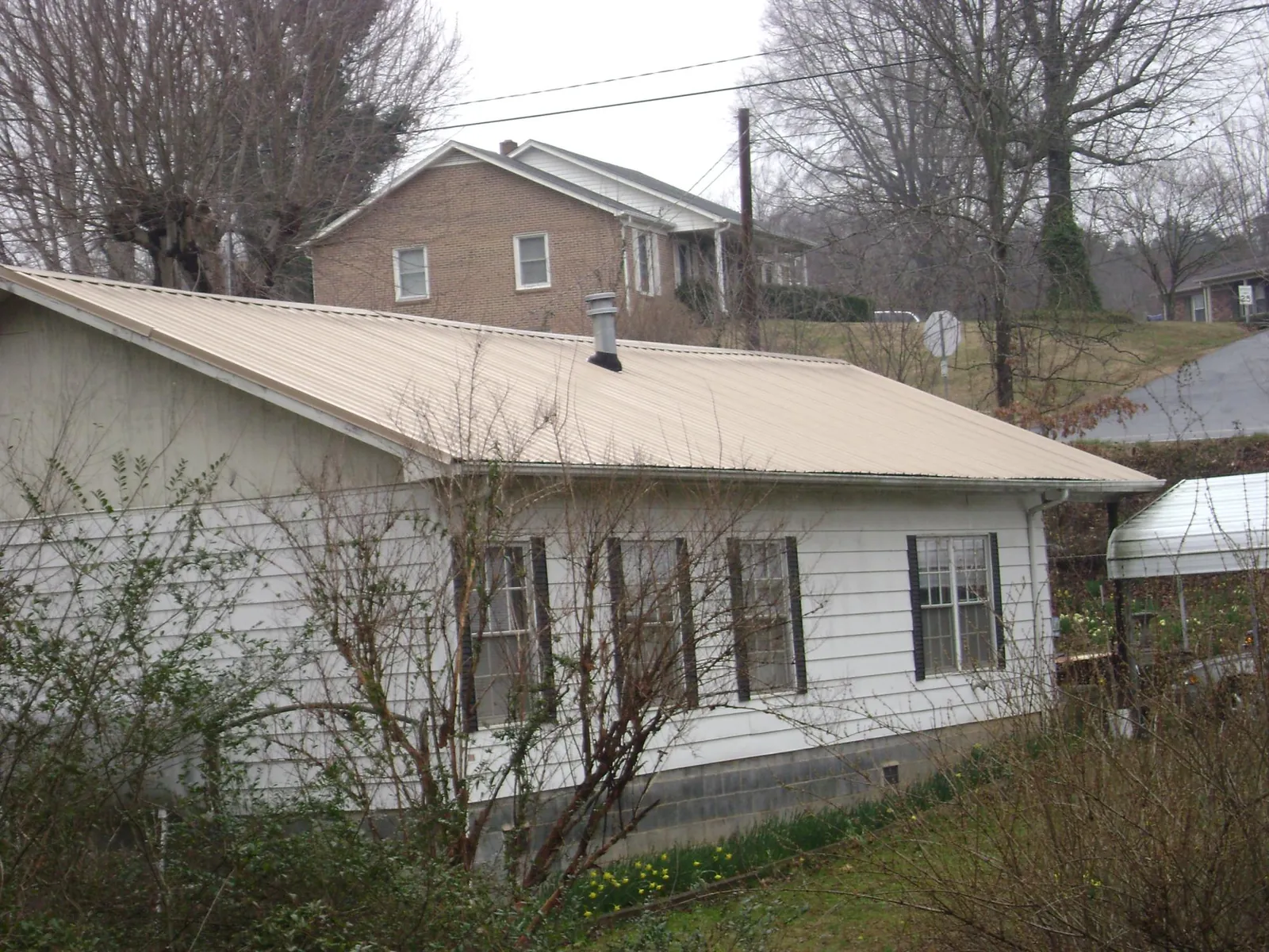 Tan metal roof on a white sided house set into a hillside — Commercial Roofing by Roofing Brothers in Revloc